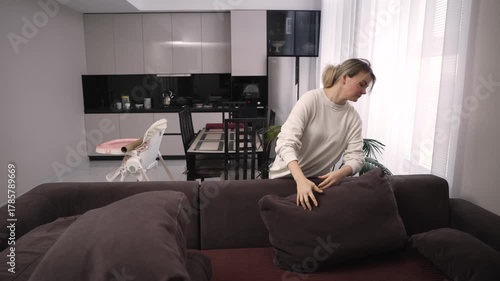 Young woman tidying up and plumping cushions on the sofa