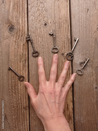 Close up of a female's hand and a few vintage keys on a wooden table.