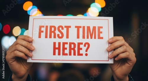 Hands hold sign asking first time here question with bokeh lights background