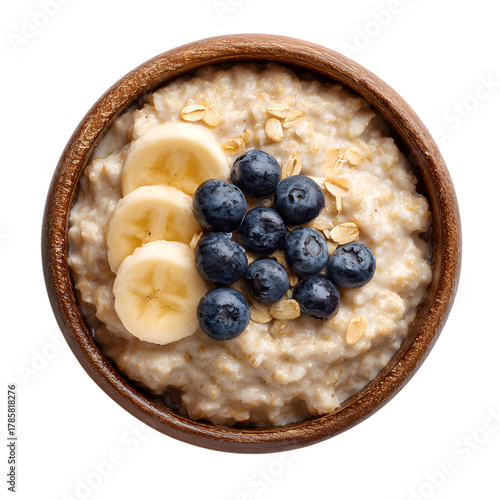 Overhead view of oatmeal with banana slices and blueberries in a wooden bowl on transparent background