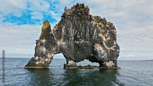Close drone view of Hvítserkur sea stack, Iceland. Dramatic basalt arch formation against blue sky and ocean.