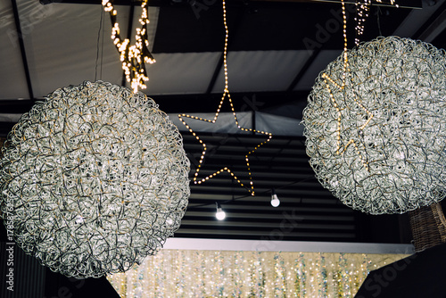Illuminated wire-frame stars and wreaths hanging from a ceiling in a modern holiday display. Christmas lighting, geometric festive decor, sculptural illumination, contemporary holiday styling