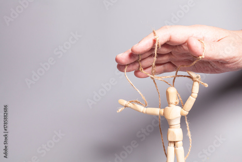 Man's hand pulling strings of wooden puppet on gray background. Concept of emotional manipulation,dictatorship and control