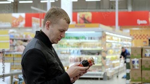 Tableau sur toile Man carefully reads juice bottle label in supermarket, making a healthy choice while shopping