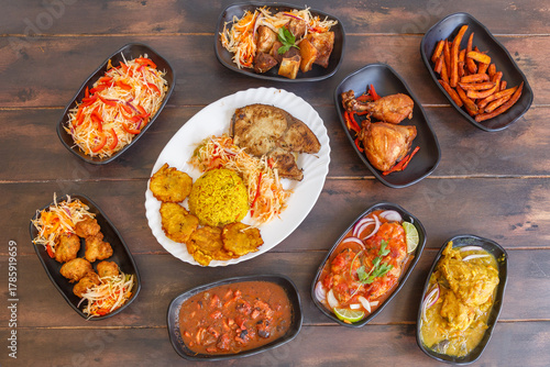 Variété de plats antillais et créoles (accras de morue, colombo de poulet, fricassée de chatrou, court-bouillon de poisson, griot de porc, pikliz, riz Djon Djon, bananes pesées) sur une table en bois 