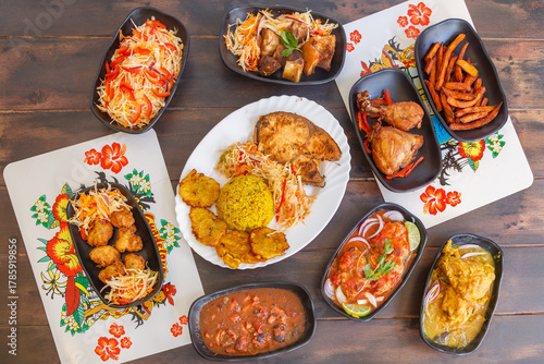 Variété de plats antillais et créoles (accras de morue, colombo de poulet, fricassée de chatrou, court-bouillon de poisson, griot de porc, pikliz, riz Djon Djon, bananes pesées) sur une table en bois 