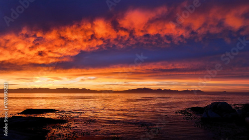 Aerial view of the horizon ablaze with fiery oranges and deep purples reflecting on the tranquil ocean waters, Cape Town, Western Cape, South Africa.