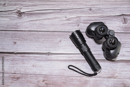 Binoculars and a flashlight on a wooden table. Black binoculars, black flashlight.