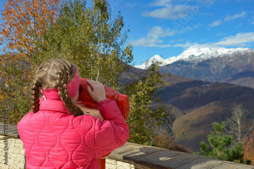 A girl in a pink jacket looks at the mountains through a binoscope. binoculars with a view of Krasnaya Polyana. The mountains of Sochi resort. a child in nature. background for the design.