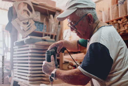 Senior artisan crafting wood in workshop using drill tool