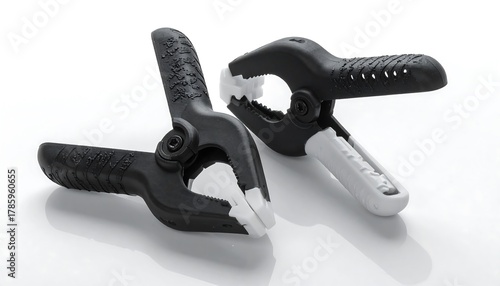 Two black and white spring clamps, positioned on a reflective surface, offering a studio-style photograph. The grips show textured design