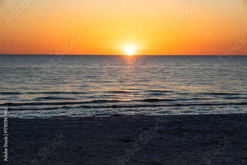 Golden sunset over calm ocean waves and sandy beach horizon