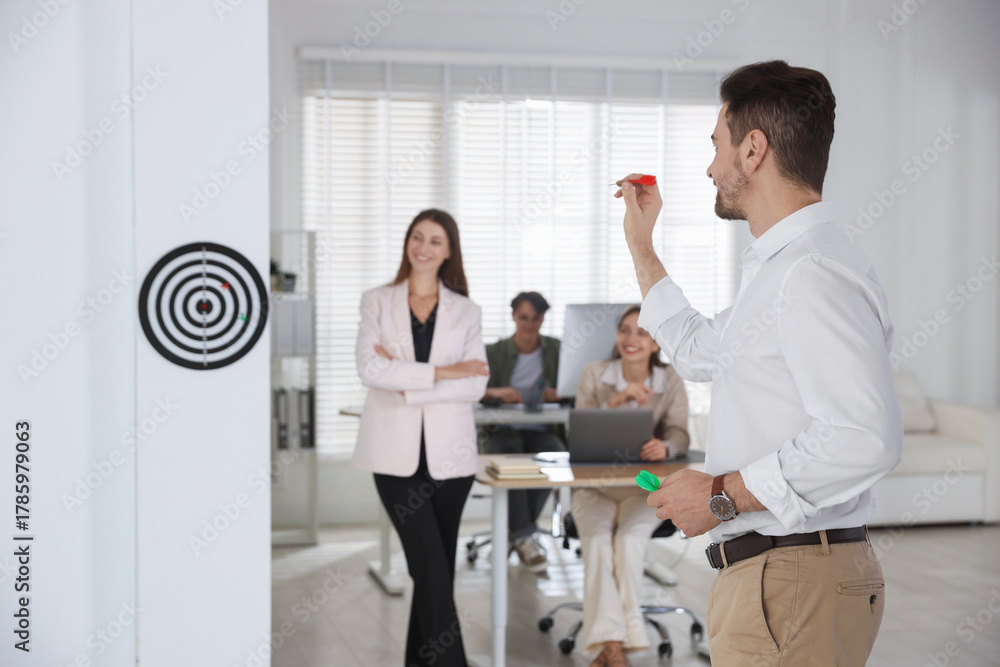 Fototapeta premium Group of colleagues playing darts in office, selective focus