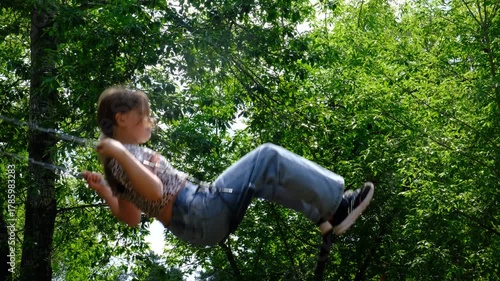 Teenage girl nestled on swing finds solace in the empty park, savours moment of unhurried day. Summer vacations, brightly lit by sunlight and set against a backdrop of lush green trees and sky.