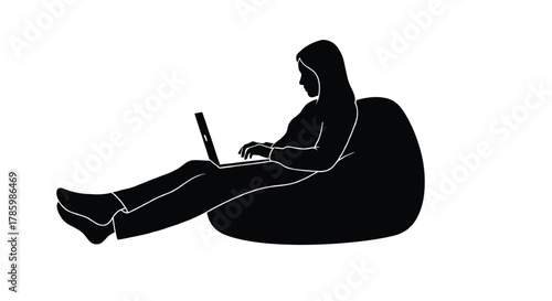 Silhouette of a person wearing a hijab sitting comfortably on a large beanbag chair and typing on a laptop computer