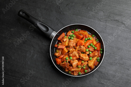Delicious cooked stew in frying pan and ingredients on black table, top view
