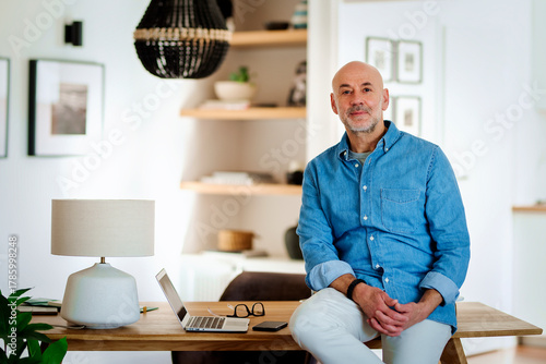 Confident middle-aged man sitting at desk at home and smiling at camera