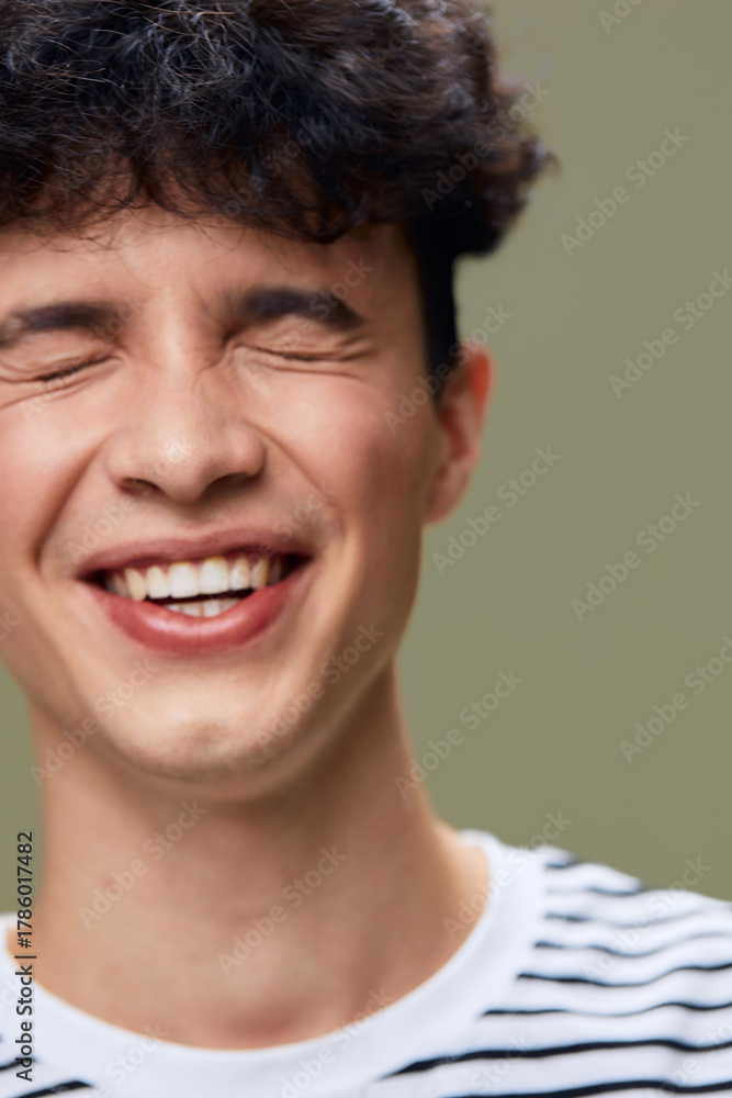 Fototapeta premium smiling man with closed eyes expressing joy and happiness, wearing a striped shirt, youthful style, natural light, green background, casual indoor portrait