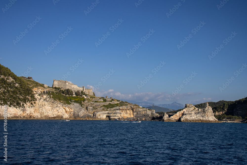 Fototapeta premium Panoramic view from the sea of ​​the historic town of Portovenere. The image highlights the Church of San Pietro and the ancient fortifications built on the rocks. Italy