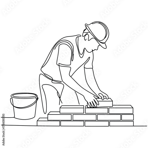 Construction worker building a brick wall with a bucket nearby