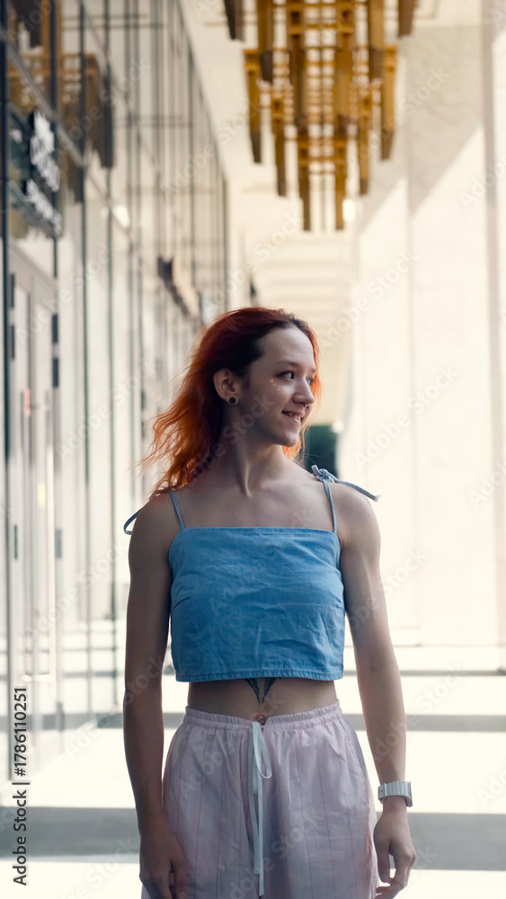 Fototapeta premium A portrait of a teenage girl with red hair posing for a photo near columns at the entrance to a business center
