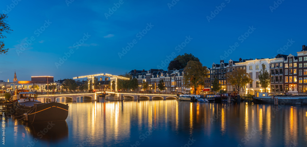 Naklejka premium Panorama of Amsterdam at blue hour, historical houses and Magere Brug (Skinny Bridge) reflected in river Amstel