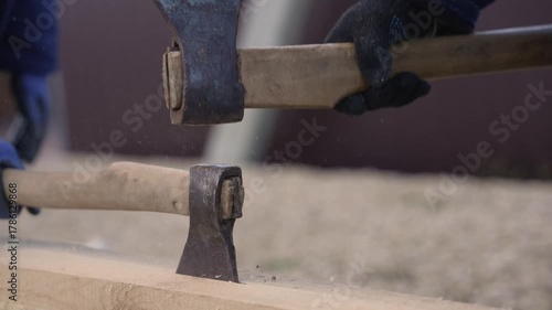 Carpenter using an axe to carve a wooden beam outdoors