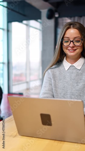 Young woman working creative on her laptop. Male colleague comes up to a lady showing his I-pad asking advice. Vertical video