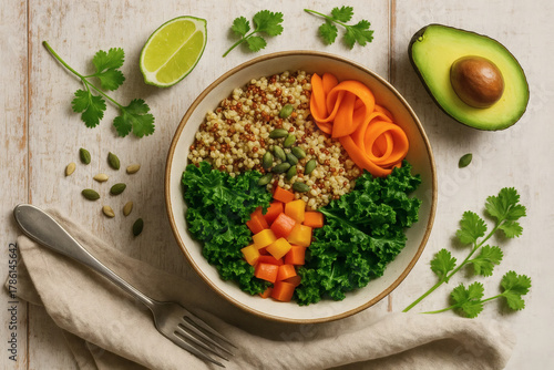 A healthy quinoa bowl with avocado, kale, carrot ribbons, mango, and pumpkin seeds, garnished with cilantro and lime, on a rustic wooden surface