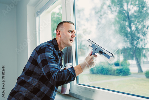 Man cleaning a window on a sunny day while wearing gloves and focused on achieving a spotless shine