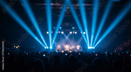 A concert stage illuminated by bright blue spotlights, with a crowd of silhouettes visible in the foreground, creating a vibrant atmosphere