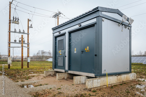 Modern electrical substation and power distribution unit installed on concrete base at a solar farm, with nearby transformers and solar panels visible in the background.