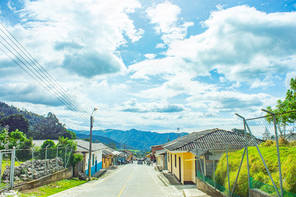 Fototapeta premium A beautiful landscape of a road in Purace, Cauca, with colorful houses and rolling hills under a clear blue sky.