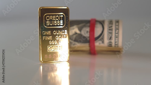 Pure 999.9 gold bullion bar from credit suisse alongside a roll of american dollar currency