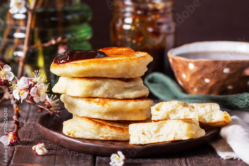 Lenten yeast pancakes with plum jam and tea, and a bouquet of blooming apricot branches on a wooden table.