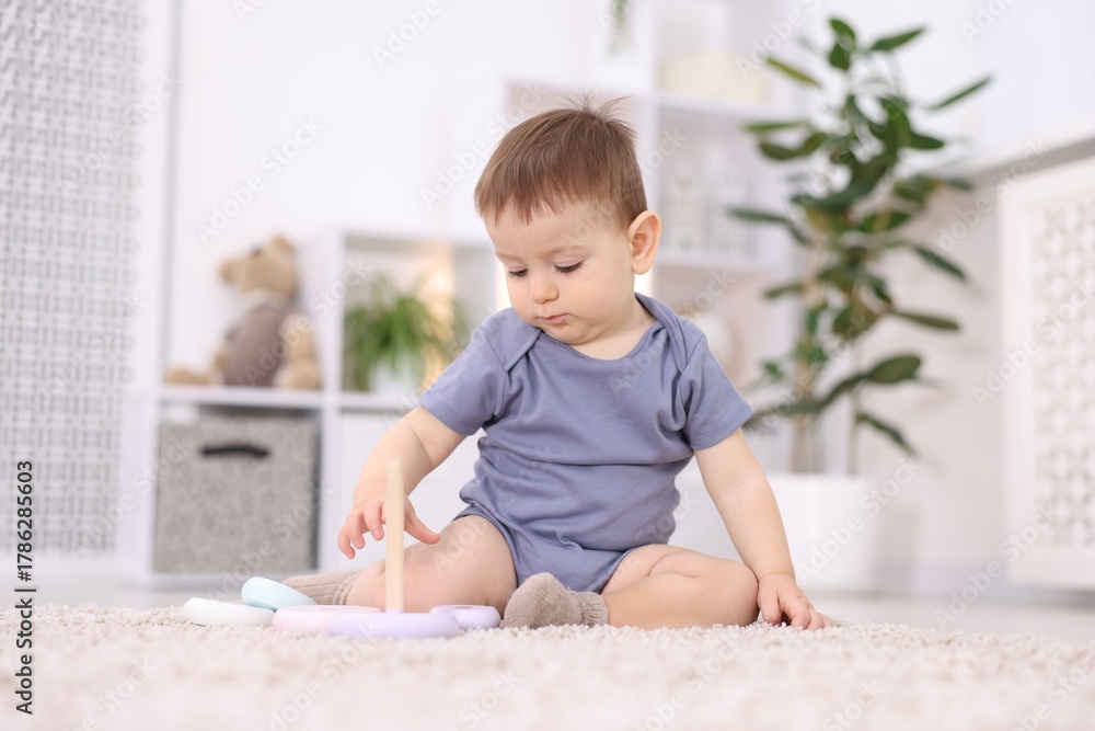 Fototapeta premium Cute little baby sitting and playing with toy on floor at home