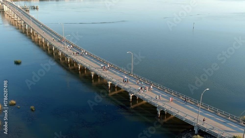 Aerial view of people doing a volksmarch or running race over a bridge surrounded by water.