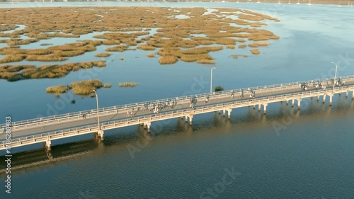 Aerial view of people doing a volksmarch or running race over a bridge surrounded by water.