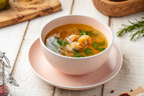 Clear homemade soup with small meatballs, noodles and parsley in ceramic bowl on wooden table