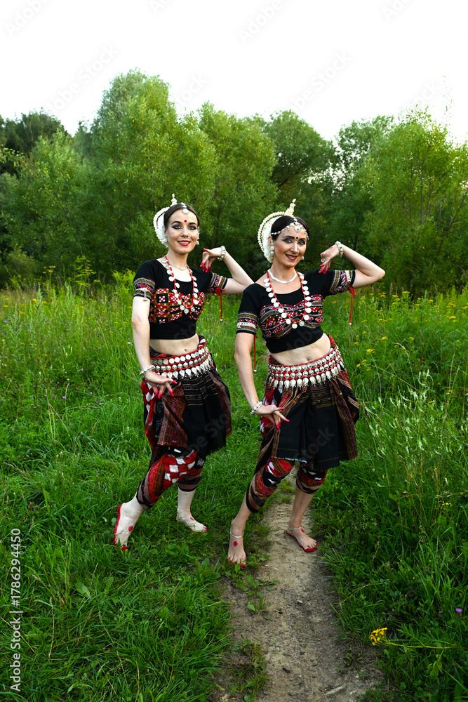 Fototapeta premium Two Indian dancers in fancy dance costumes outdoors against the backdrop of nature and forestTwo Indian dancers in fancy dance costumes outdoors against the backdrop of nature and forest