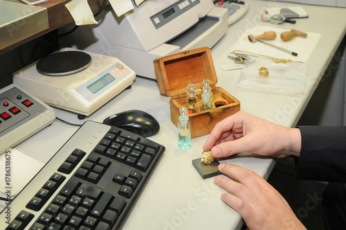 Closeup of a person's hands checking the purity of a gold jewel on a table.