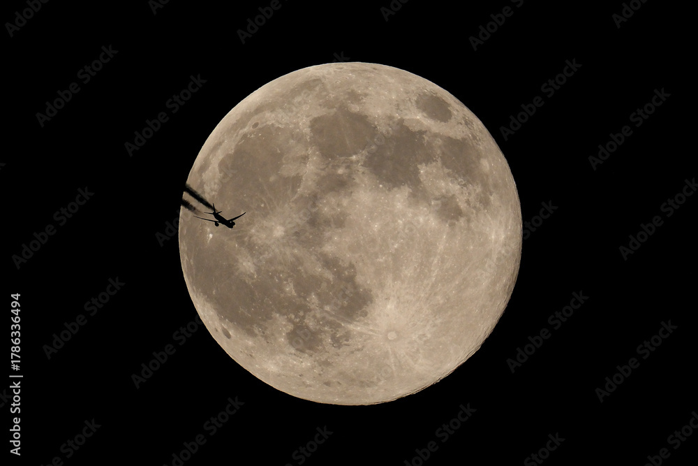 Fototapeta premium The moon and an airplane in the night sky. The plane is flying across the moon, against a black background.