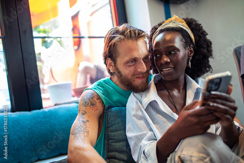 Young couple cuddling affectionately while browsing smartphone at cozy cafe