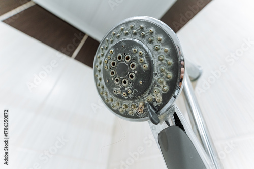 Cleaning limescale from shower fixtures, Homeowner removing mineral deposits from shower heads, Closeup of clogged shower nozzle with mineral buildup and homeowner performing cleaning tasks