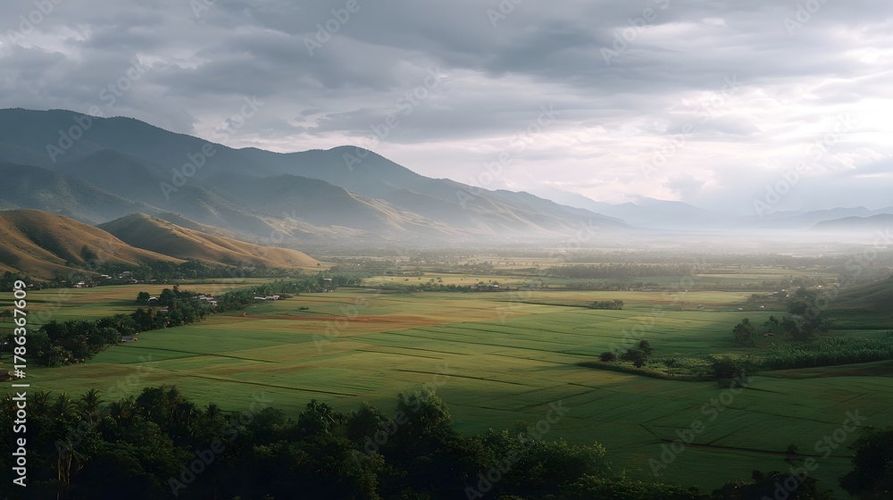 Obraz premium Misty valley landscape with rolling hills agricultural fields and distant mountains under atmospheric light