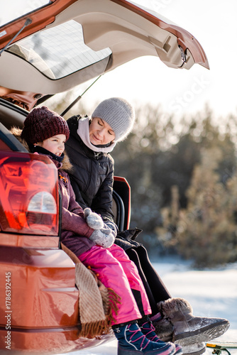 A mother and daughter are drinking tea in the winter forest, sitting in the open garage of their car.