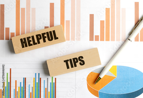 Wooden blocks with the words helpful tips on financial charts background with pen, representing advice
