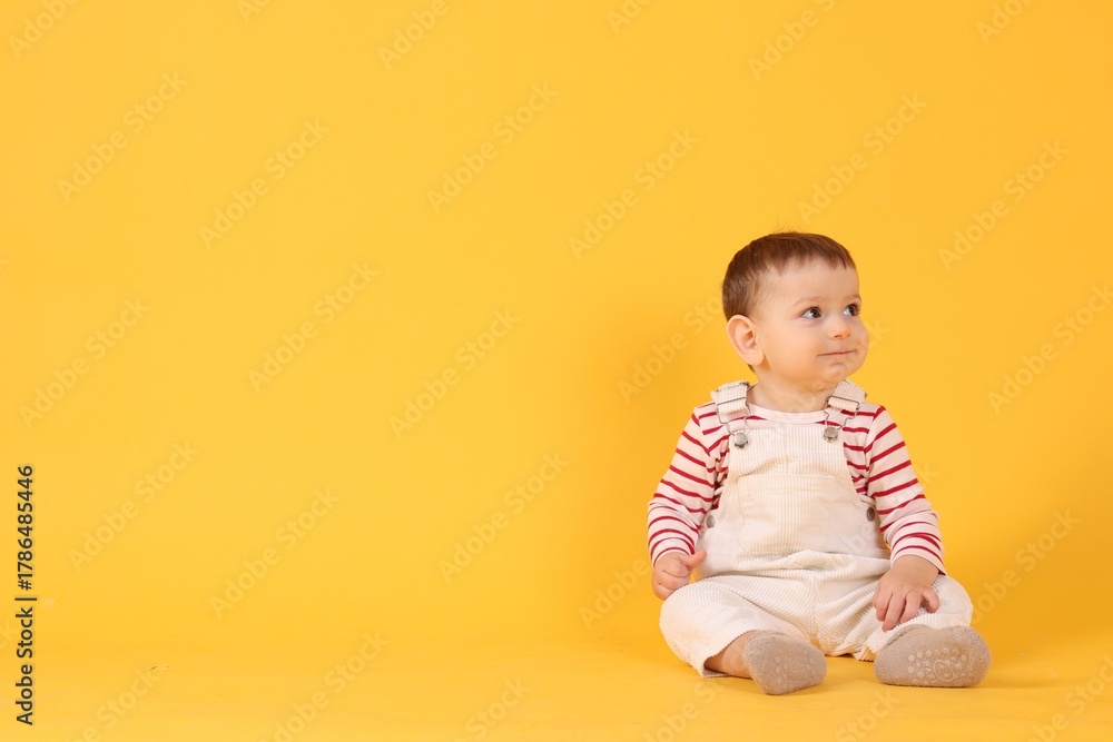 Naklejka premium Cute little baby sitting on yellow background, space for text