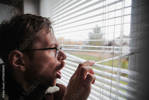 Angry man in glasses peeking through window blinds. Spying on the neighbors. Problems with the neighborhood.