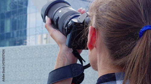 Young woman photographer with a professional camera taking pictures of a modern office building, capturing urban landscapes and architectural details from a creative perspective outdoors